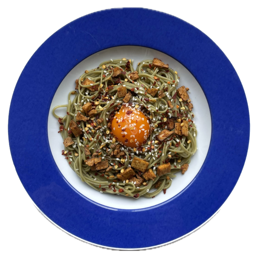 Green soba with cured yolk, sesame and chili on a blue plate